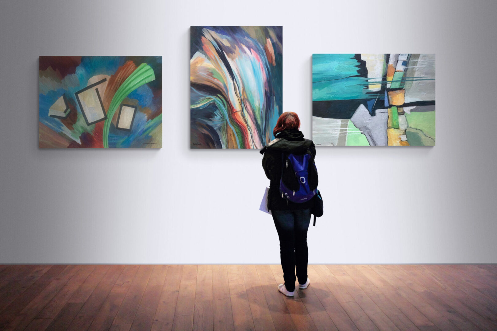 A woman looking at three abstract paintings in a local art gallery.