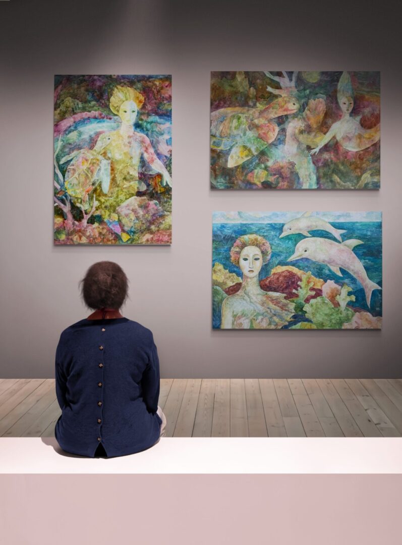 A man sitting on a bench surrounded by local fine art paintings for sale.